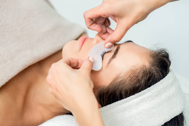 Kosmetologin kädet asettavat nauhat nuoren naisen silmän alle ennen silmäripsien pidennysmenettelyä, lähennä
. - Valokuva, kuva