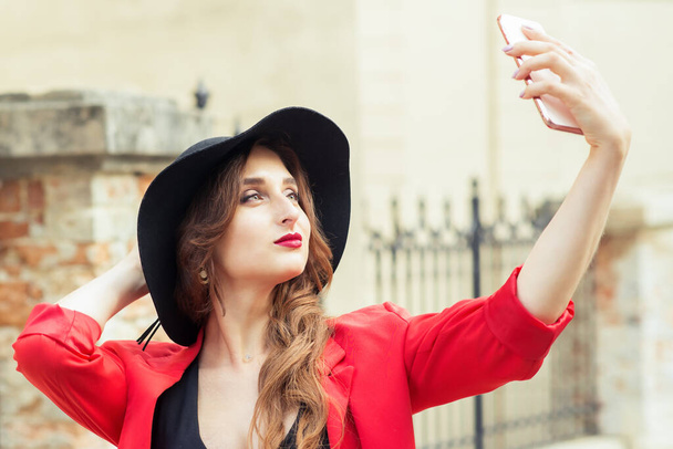 Close up portrait of a beautiful young woman is posing and makes selfie. Beauty girl makes selfie for her smartphone. Outdoors portrait of woman. - Photo, Image