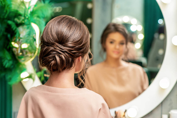 Rückansicht der hübschen brünetten jungen Frau mit Frisur vor dem Spiegel im Schönheitssalon. - Foto, Bild