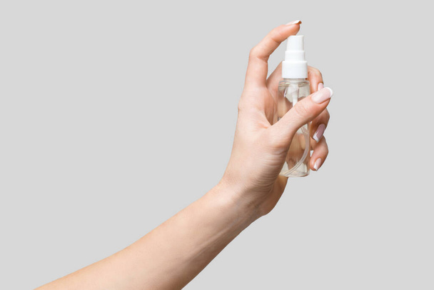 Female hands using hand sanitizer spray dispenser over light grey background - Foto, imagen