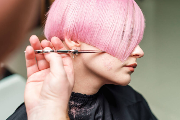 close up hands of professional hair stylist are cuting pink hair with scissors, concept beauty salon, female hairdresser - Photo, Image
