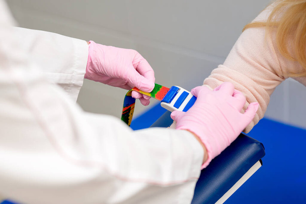 Enfermera aprieta el arnés en el brazo para extraer sangre de una vena para su análisis
. - Foto, Imagen
