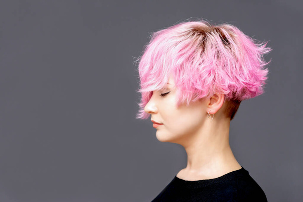 ピンクの髪型の女性は、コピースペースとグレーの背景に閉じた目の側のビューで立っています。トーン. - 写真・画像