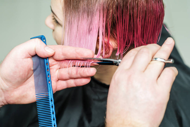 Peluquería masculina está cortando el pelo rosa de la mujer de cerca
. - Foto, Imagen