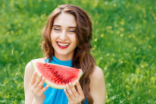 Portrait of smiling girl with slice of watermelon on background of green grass. Smiling young woman holds piece of red watermelon with copy space. - Photo, Image