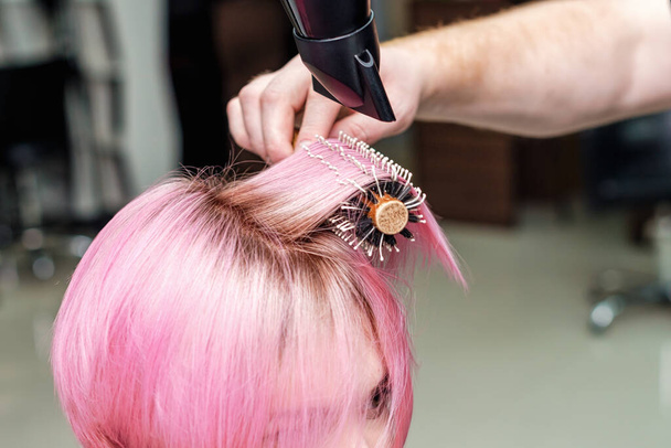 Friseur trocknet rosa Haare mit Fön und Rundbürste. Friseur föhnt kurze rosa Frauenhaare aus nächster Nähe. - Foto, Bild