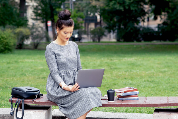 Una estudiante usa un portátil en el banco del parque. Chica está trabajando en el ordenador portátil y estudiar mientras está sentado en un banco en el parque
. - Foto, imagen