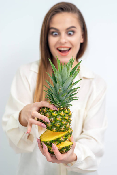 Pineapple in section in hands of beautiful young woman with surprised facial expression on white background. - Fotó, kép