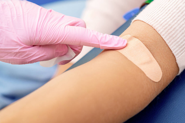 Doctor in rubber protective gloves glues an adhesive bandage on arm. - Photo, Image