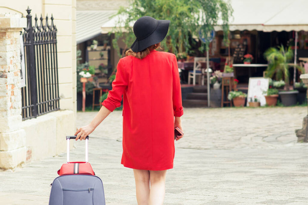 Podróże kobieta w czarnym kapeluszu spacery z walizką na ulicy miasta. - Zdjęcie, obraz
