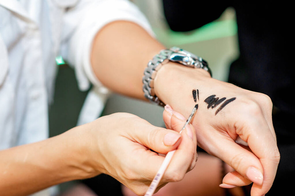 close-up make-up kunstenaar test de zwarte cosmetica met een borstel op haar hand. - Foto, afbeelding