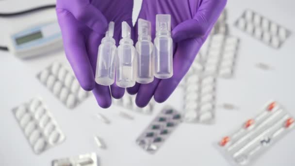 Neljä muovista lääketieteellistä ampullia käsissä suojakäsineissä lääketieteellisten laitteiden ja lääkkeiden taustalla
 - Materiaali, video