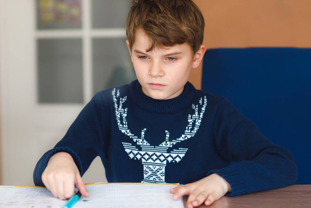 Hard-working happy school kid boy making homework during quarantine time from corona pandemic disease. Healthy child writing with pen, staying at home. Homeschooling concept - Foto, Imagen