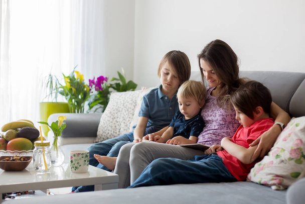 Jeune femme, mère avec trois enfants, lecture d'un livre à la maison, câlins et rires, bonheur familial - Photo, image