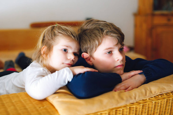Cute little toddler girl and school kid boy watching animal movie or movie on tv. Happy healthy children, siblings during coronavirus quarantine staying at home. Brother and sister together. - Foto, Imagen