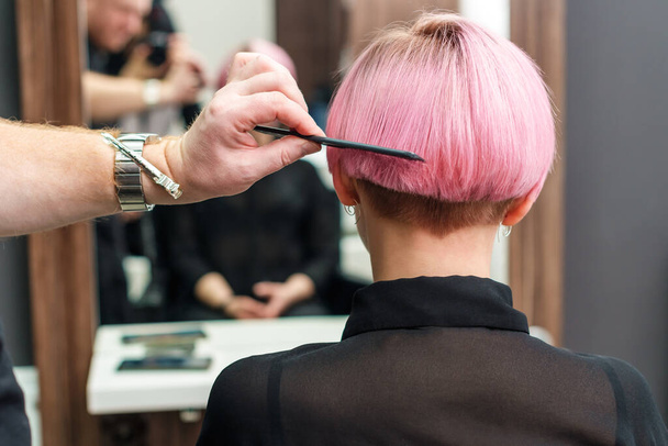 Primer plano de una peluquera peina el pelo corto de color rosa de su cliente en el salón de belleza. Concepto de cuidado del cabello profesional
. - Foto, Imagen