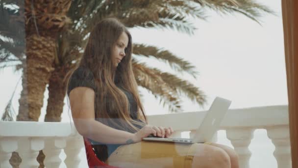 Schöne Studentin oder Freiberuflerin, die an einem Laptop arbeitet, Frau auf Balkon mit Blick auf Palme und Meer, schnelle Videos, Zeitlupe, 4k - Filmmaterial, Video