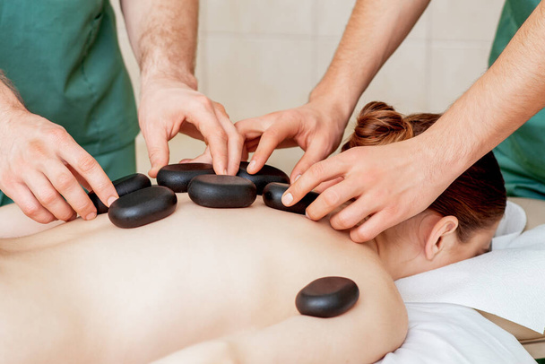 Masaje de espalda de mujer con piedras calientes negras por masajista terapeuta masculino
. - Foto, imagen