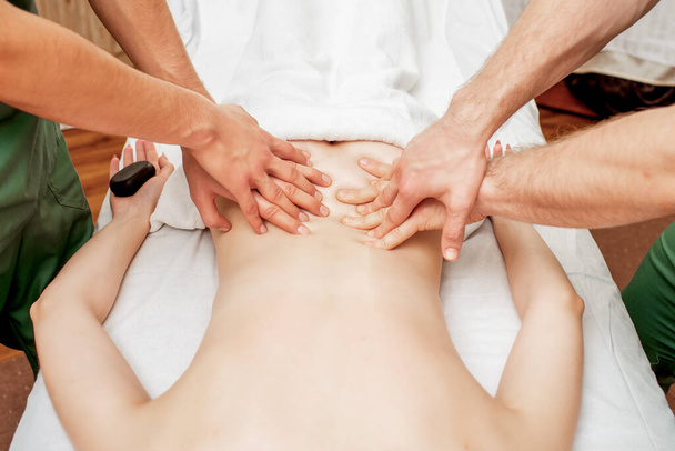 Woman receiving back massage with four hands of two male therapists close up. - Фото, изображение
