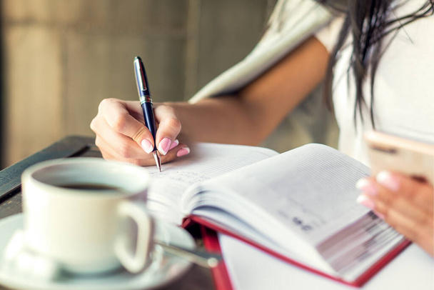 Giovane donna mano destra scrittura piani su piccolo diario in caffè da vicino. Concetto aziendale
 - Foto, immagini