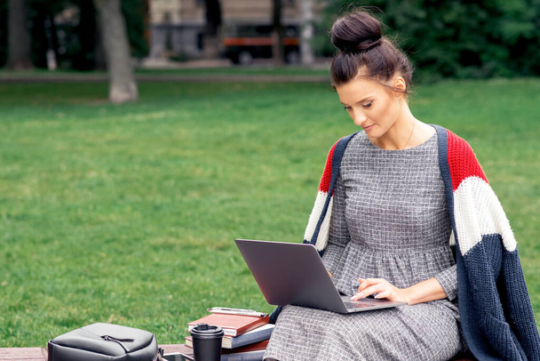 Estudiante chica está utilizando el ordenador portátil en el parque. Mujer está trabajando en el ordenador portátil y estudiar mientras está sentado en un banco en el parque
. - Foto, imagen