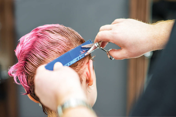 Primer plano de las manos están cortando el cabello rosa húmedo del cliente en la peluquería. Peluquería corta el pelo de la mujer. manos peluquero cortes de pelo rosa
. - Foto, imagen
