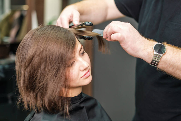 Coiffeur professionnel lissage cheveux bruns avec lisseurs dans le salon de beauté
 - Photo, image