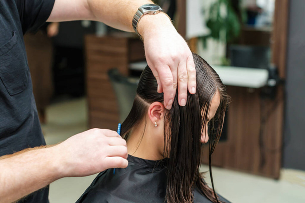 Парикмахер расчесывает влажные волосы женщины в парикмахерской
. - Фото, изображение