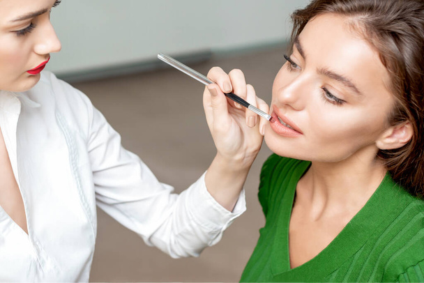 Maquillaje artista aplica lápiz labial en los labios de la mujer, maquillaje en proceso
. - Foto, imagen