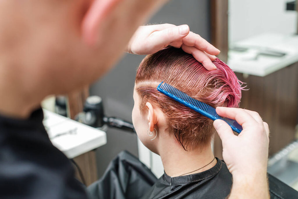 Fryzjer używa grzebienia dla kobiet różowe włosy w salonie fryzjerskim. Mężczyzna ręka jest czesanie kobiety krótkie różowe włosy w salonie piękności. Zamknij się.. - Zdjęcie, obraz