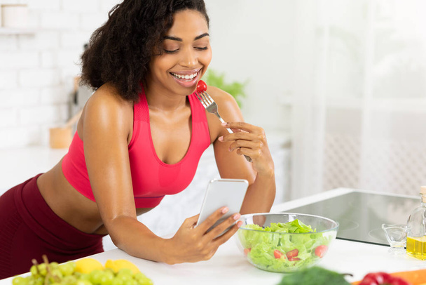 Zwart meisje met smartphone en salade eten - Foto, afbeelding