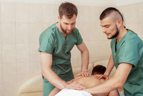 Man receiving back massage in four hands by two male therapists. - Photo, Image