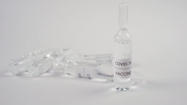 Coronavirus vaccine and COVID-19. A hand in protective blue gloves sets an ampoule with medicine on a white table. Viral infection treatment - Video, Çekim