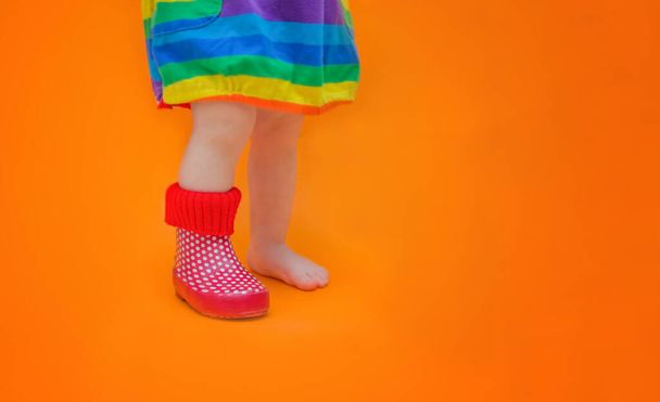 Childrens foot in one rubber boot. One leg is bare - barefoot. Baby lost her boot. The concept of spring, summertime, colorfulness and the first steps of a toddler. - 写真・画像