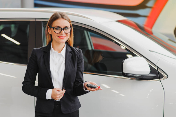 auto business, car sale, consumerism and people concept - happy woman taking car key from dealer in auto show or salon. - Photo, Image