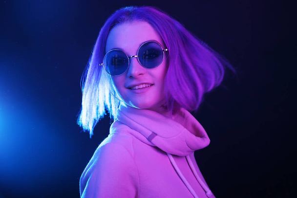 Portrait of a young woman with purple hair and sunglasses in a neon light, nightlife. Generation Y, millennials - Foto, afbeelding