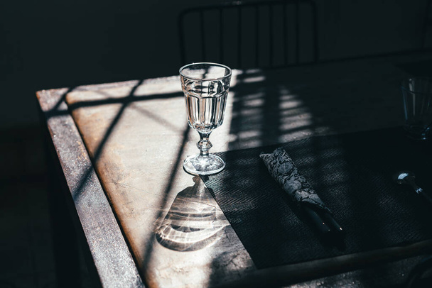 A glass goblet on a leg stands on a table among the shadows in the sunlight - Φωτογραφία, εικόνα