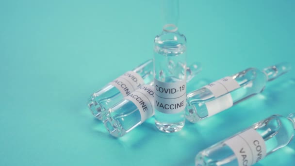 Koronavirová vakcína. Ruka v ochranných lékařských rukavicích zvedne ampulku mimo jiné na modrém povrchu. Lék na COVID-19 - Záběry, video