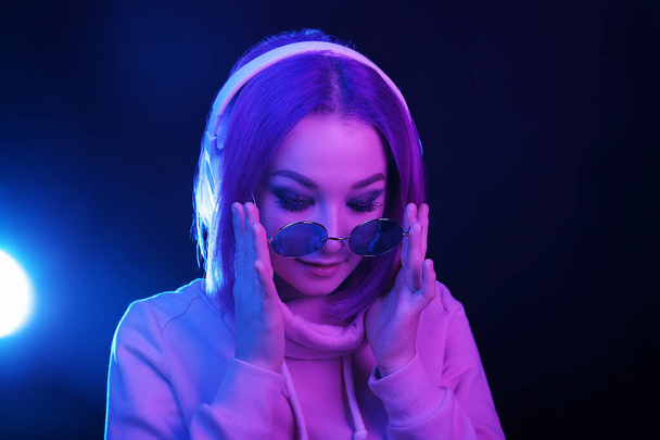 Portrait of a young woman with purple hair and sunglasses in a neon light and headphones. Night life. Generation Y, millennials. - Foto, Imagem