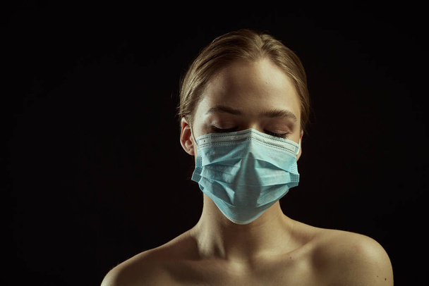 Dramatic light illustration of coronavirus epidemic. Girl with protective mask. Black background. Concept of quarantine. - Foto, afbeelding