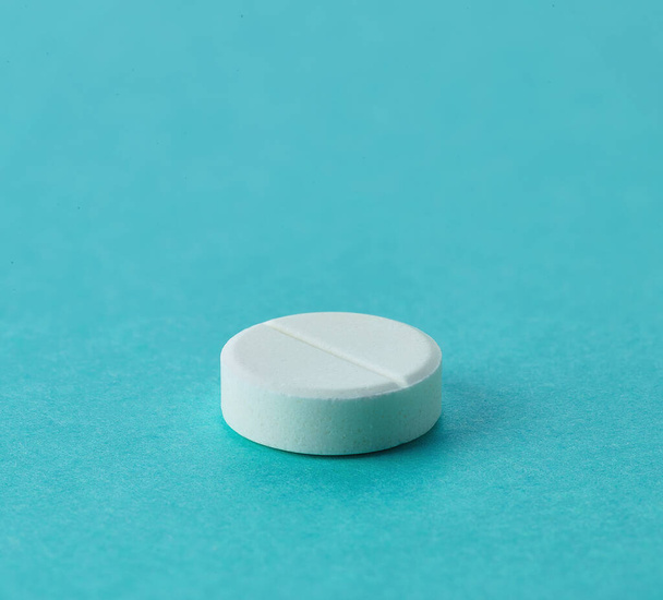 Uma pílula de paracetamol redonda branca no fundo azul com espaço vazio para texto
 - Foto, Imagem