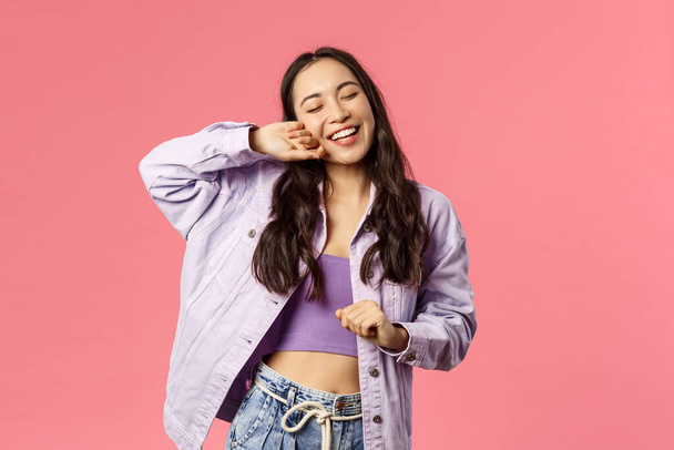 What a beautiful day. Portrait of enthusiastic, happy kawaii girl, smiling enjoying weekends, dancing with closed eyes relaxed pleased face, having fun, have no worries, pink background - Фото, изображение