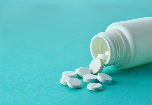 Weiße runde Medikamentenpillen, die aus einer Flasche auf blauem Hintergrund austreten - Foto, Bild