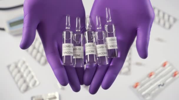 Coronavirus vaccine. Hands in protective gloves show ampoules with medicine on the background of a table with medical equipment and capsules. The medicine for COVID-19 - Кадри, відео
