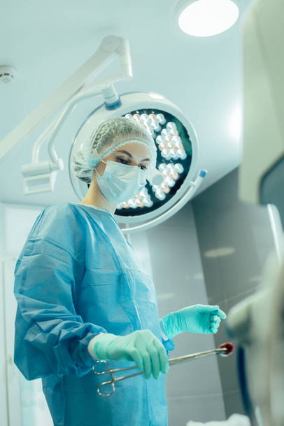Erfahrener Arzt hält während des chirurgischen Eingriffs ein Stück Watte mit einer Pinzette - Foto, Bild