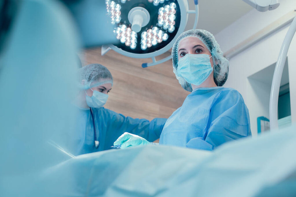 Woman in a medical mask working with colleagues in the operating room - Foto, afbeelding