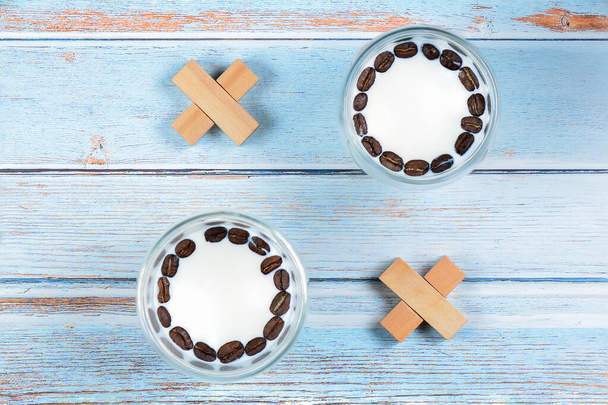 Σκέψεις και σταυροί από ποτήρια με γάλα και φασόλια καφέ, μικρά ξύλινα τουβλάκια σε ανοιχτό μπλε φόντο ξύλου - Φωτογραφία, εικόνα
