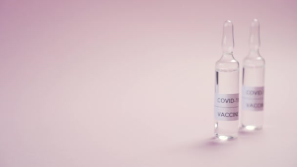 Vacina contra o coronavírus e da COVID-19. Uma mão em luvas de proteção coloca a ampola com o medicamento em uma superfície rosa. Tratamento da infecção viral
 - Filmagem, Vídeo