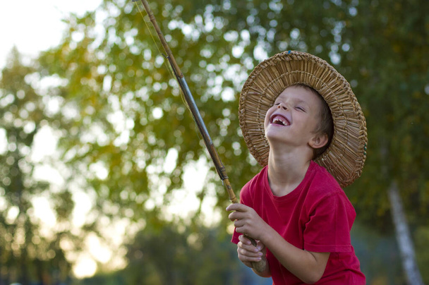 7 éves fiú áll egy horgászbottal a háttérben a természet és nevet boldogan - Fotó, kép