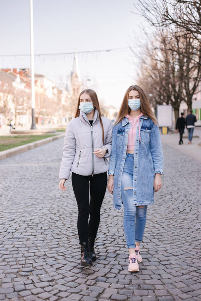 Κορίτσια με μάσκες. Θέμα του Coronavirus. Γυναίκες στην πόλη περπατούν κατά τη διάρκεια της καραντίνας - Φωτογραφία, εικόνα